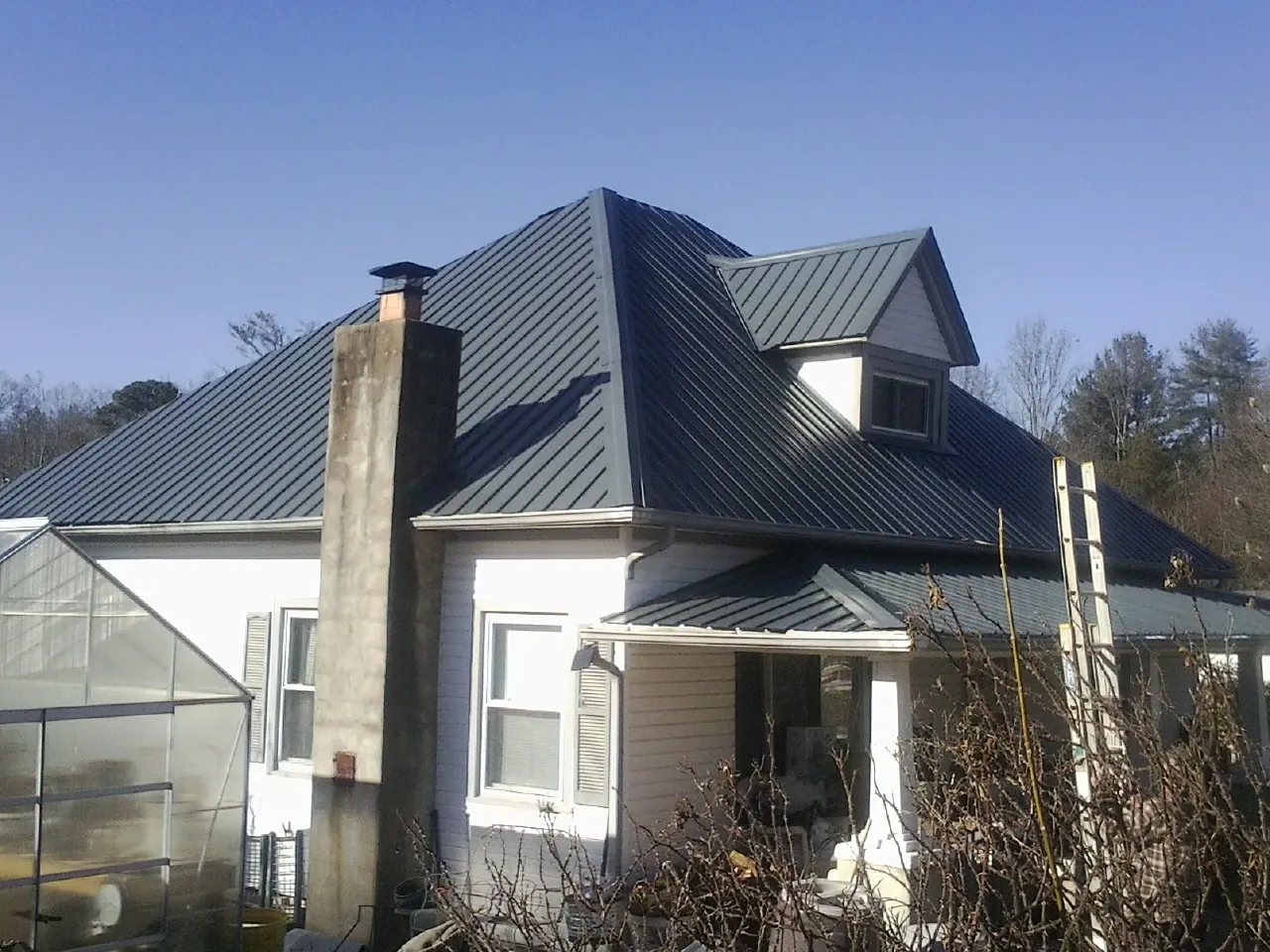 Dark blue standing seam metal roof on a white farmhouse with dormer — Slate & Tile Roof Repair by Roofing Brothers in Sigourney