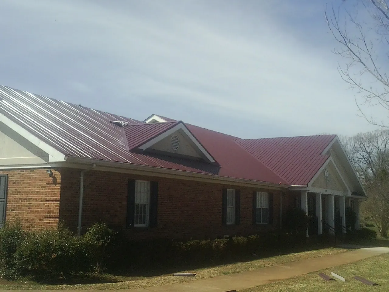 Red metal roof with gabled entries on a long brick building, from a Hail Damage Roof Repair job in Sigourney