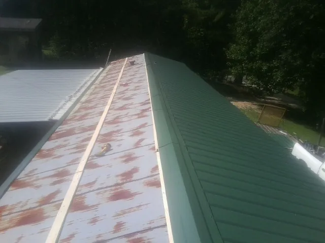 Old rusted panels beside newly installed green metal roofing — Wind Damage Roof Repair by Roofing Brothers in Sigourney
