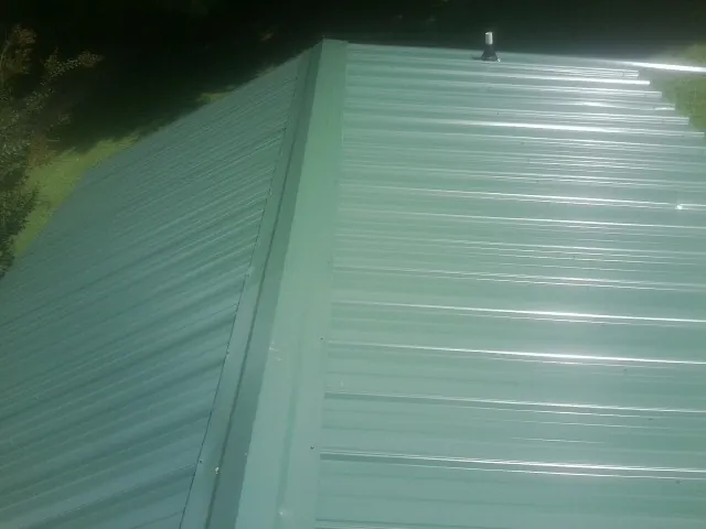 New green metal panels meeting at the ridge of a roof — Flat Roof Repair work by our crew in Sigourney