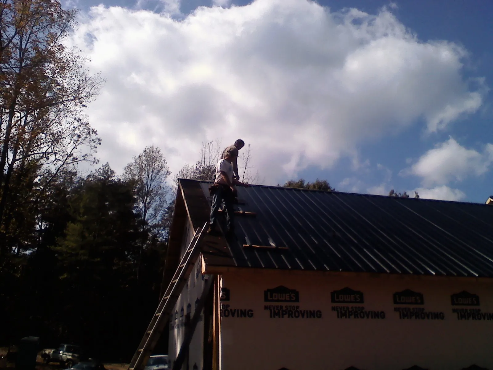 Roofer fastening dark metal panels high against a cloudy sky, from a Roof Inspection job in Sigourney