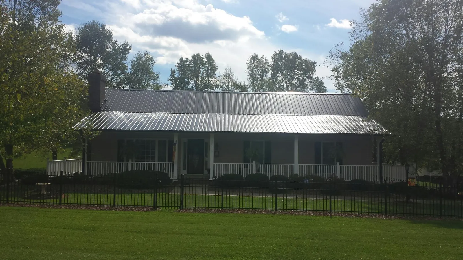 Gray metal roof on a brick ranch with a full width front porch — Gutter Guard Installation work by our crew in Sigourney