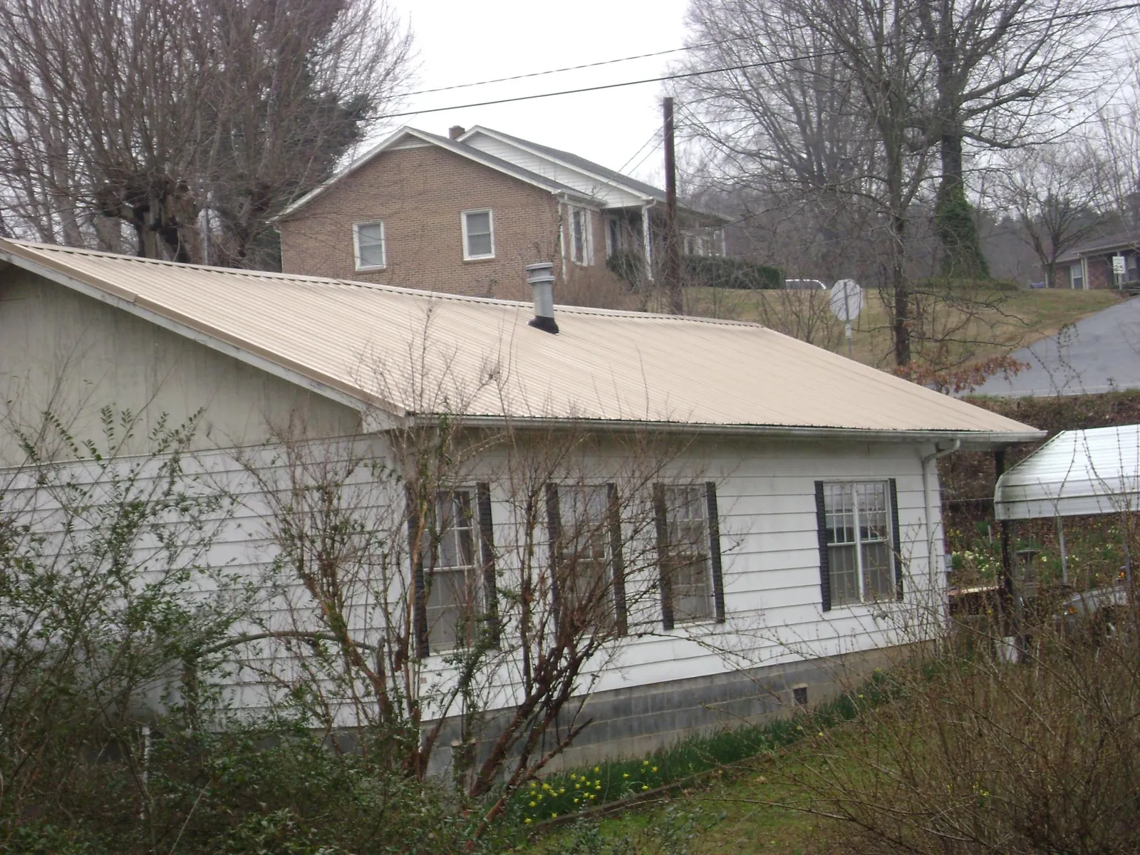 Tan metal roof on a white sided house set into a hillside — Commercial Roofing by Roofing Brothers in Sigourney