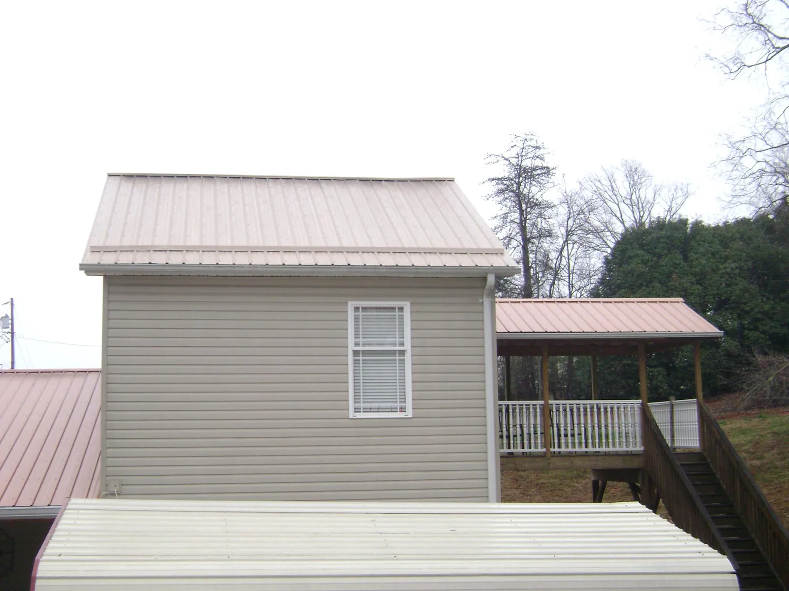 Tan metal roofs on a two story addition and attached porch, from a Roof Replacement job in Sigourney