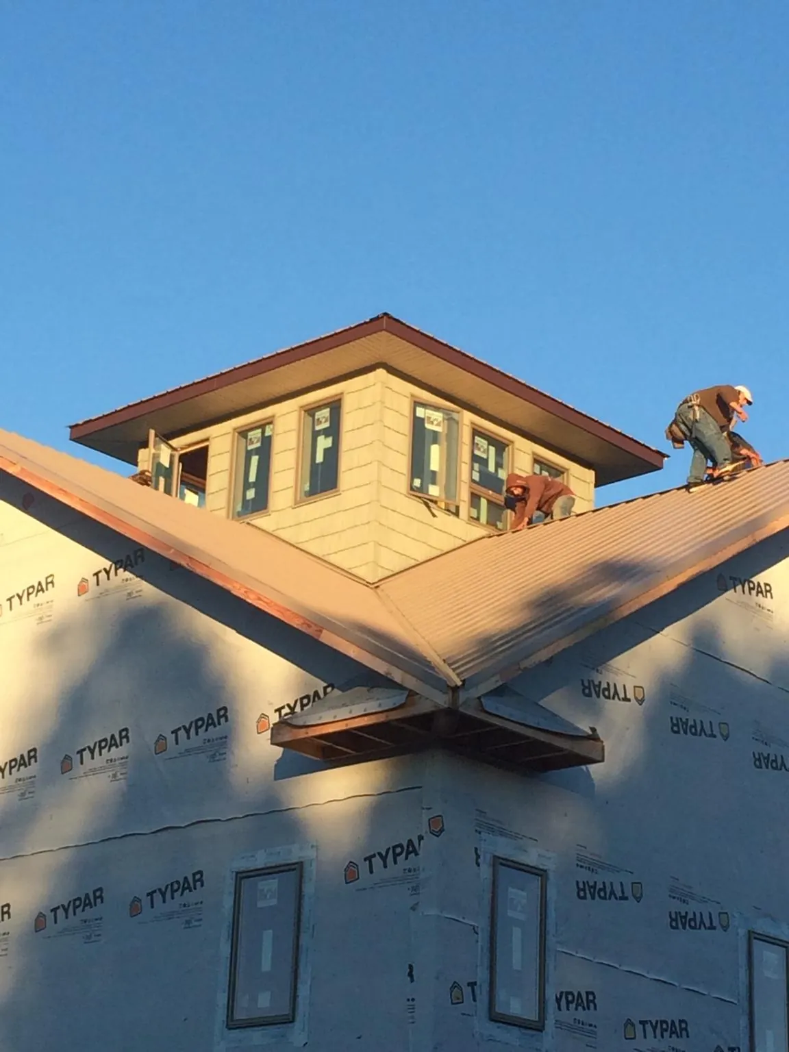 Roofers working around a rooftop cupola on a new metal roof at sunset — Roof Waterproofing in Sigourney by Roofing Brothers
